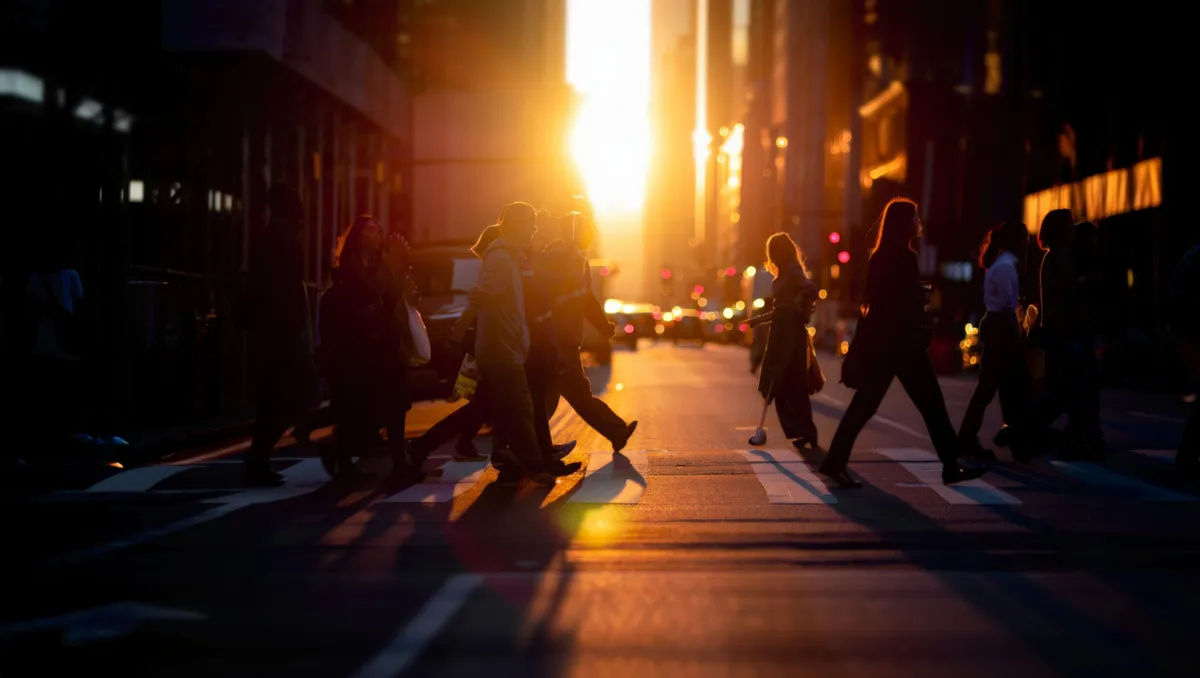 Menschen überqueren bei Sonnenuntergang eine Straße zwischen Hochhäusern